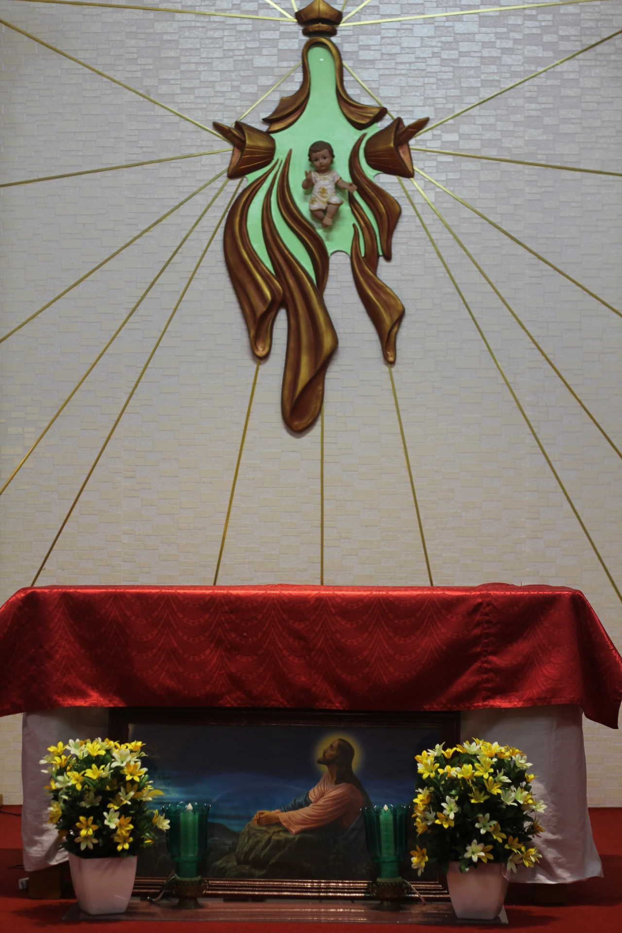 An altar beneath a religious wall sculpture in a prayer space.